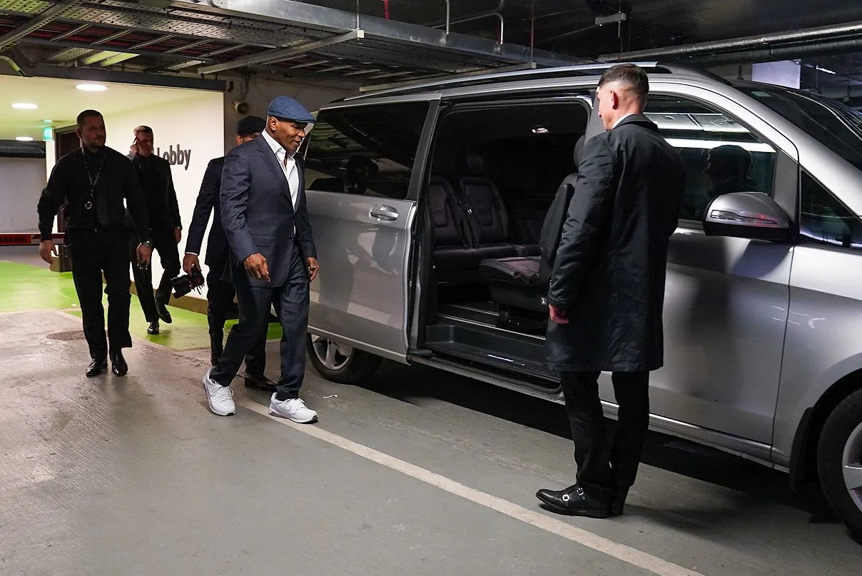Executive driver and protection team assisting a passenger beside a vehicle